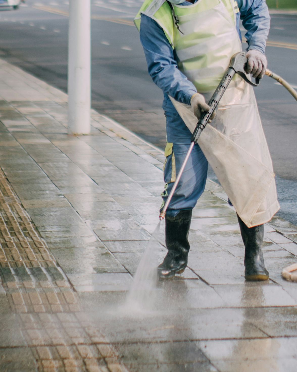 a man in a yellow vest is spraying water on a sidewalk